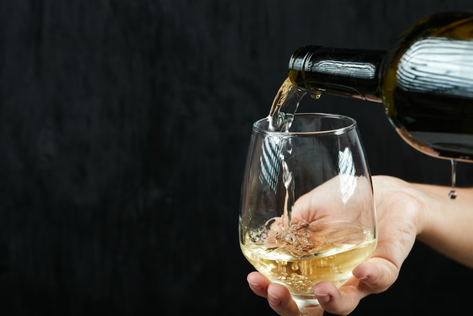hands pouring white wine into the wine glass on a dark background