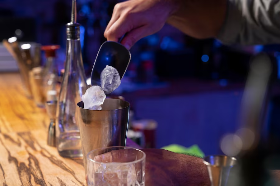 Bartender adding ice to a shaking cocktail cup