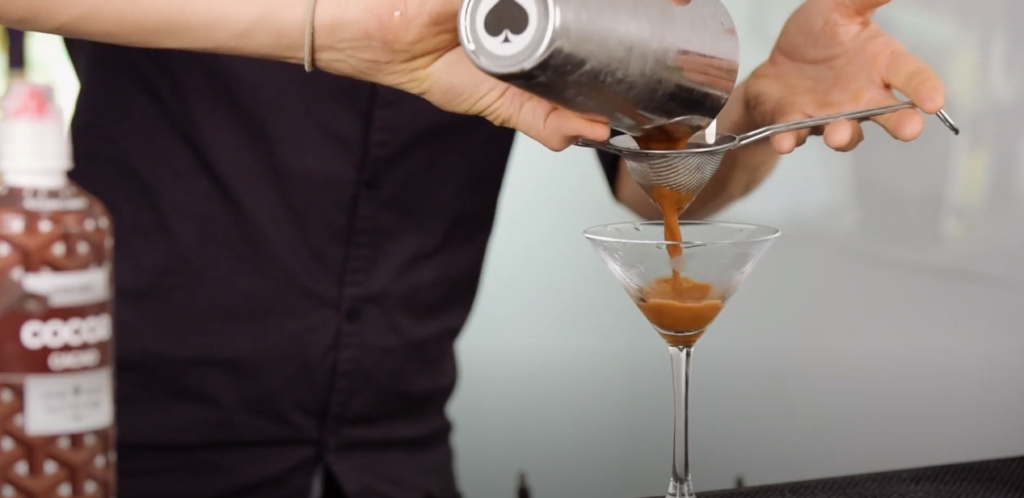 Man pouring a cocktail through a strainer into a wineglass