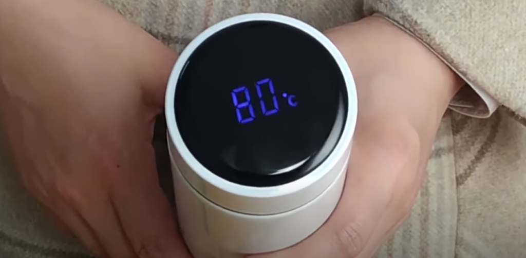 A hand holding a smart tumbler displaying the temperature