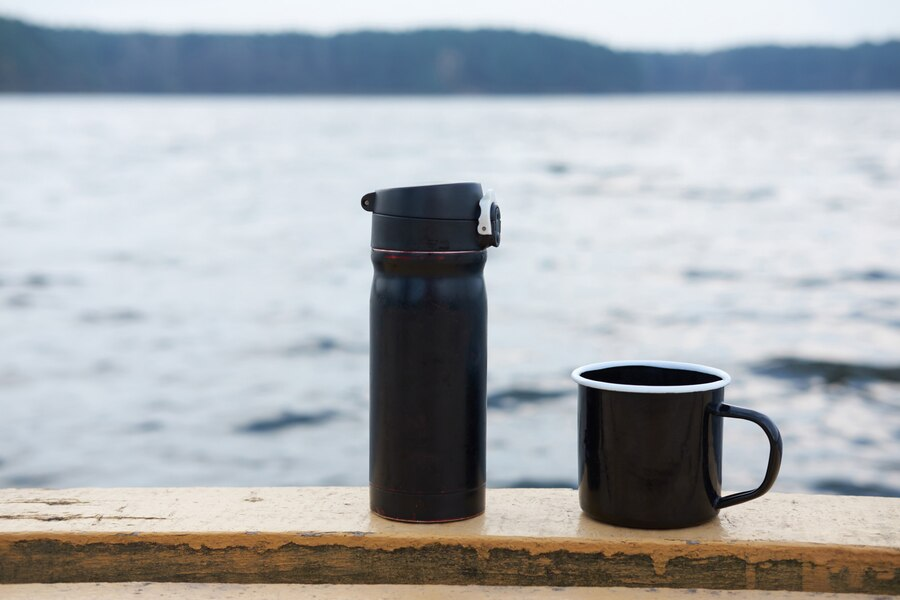 A tumbler and a mug next to each other with a beach in the background