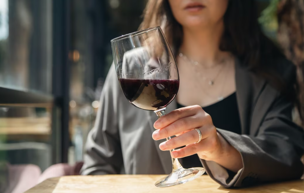 woman in a gray jacket sitting at the table and swirling the wine glass with red wine in it