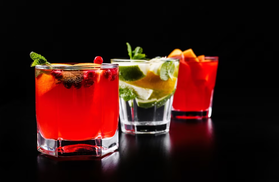 three cocktails with lemon, orange, and mint on a black background