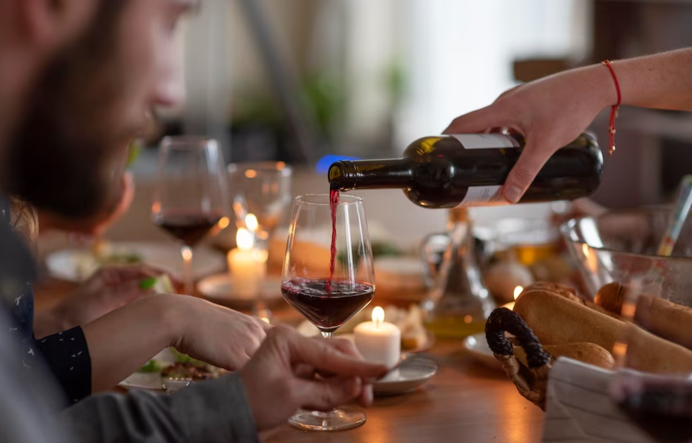 people sitting at the table, hand pouring wine for man’s wine glass, candles on the table