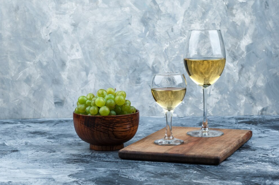 blue marble surface, bowl with grape, and two wine glasses on wooden board
