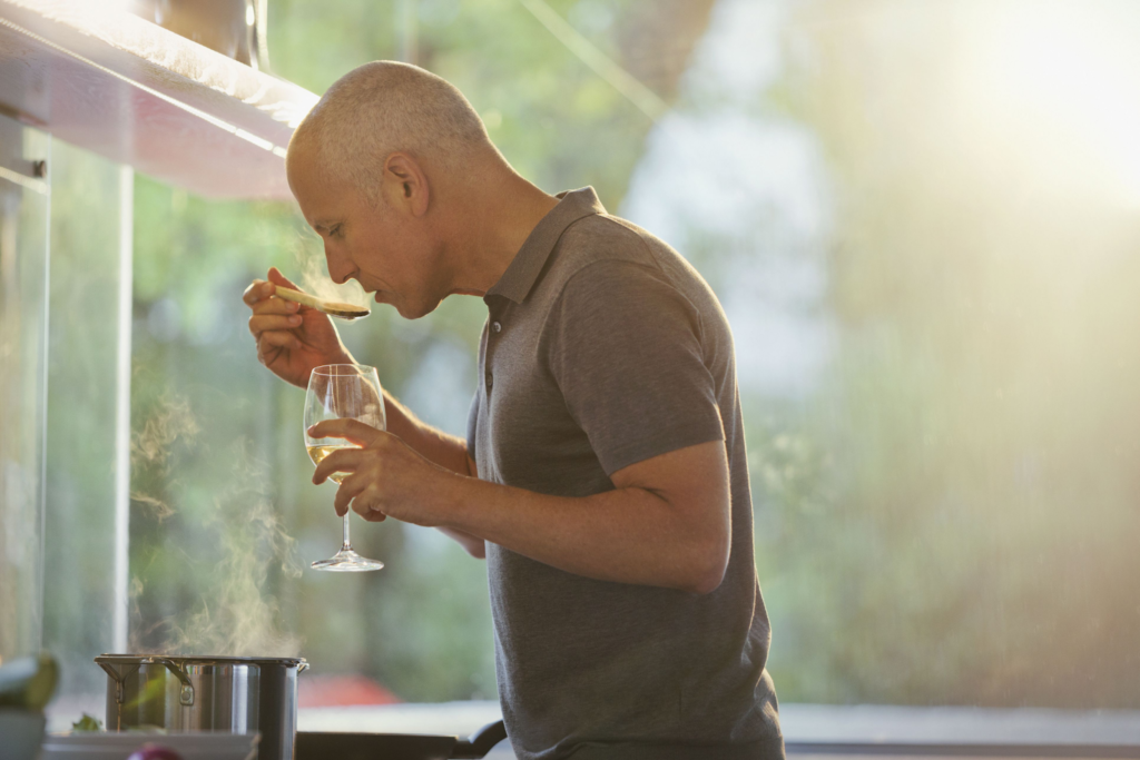 Man preparing food and holding a glass of wine